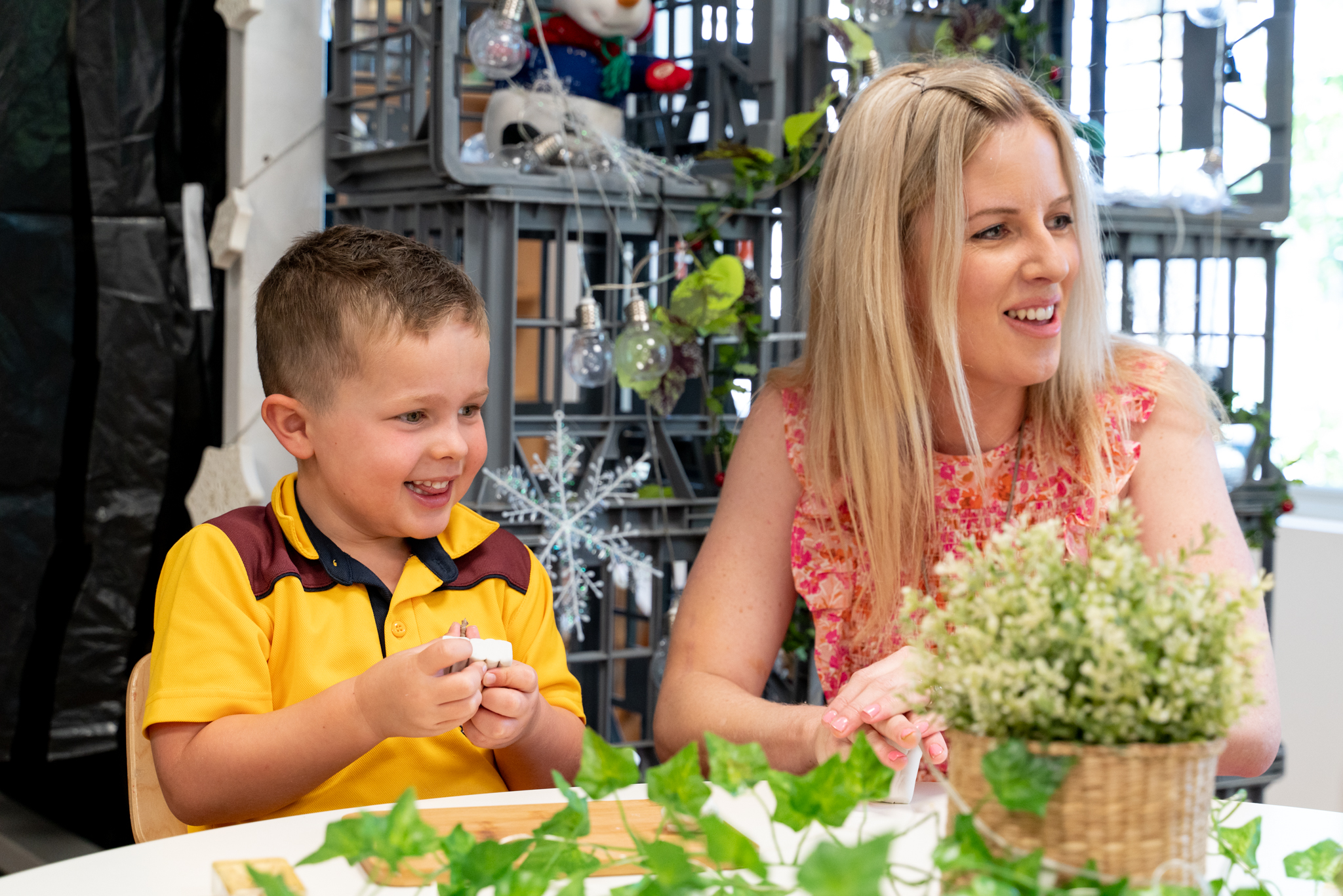 A young smiling student sat beside their teacher plays with clay at Scotch College, one of the top primary schools in Perth.